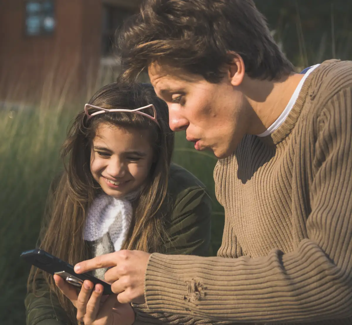 Agenturbild, das einen Vater mit seiner TOchter zeigt. Er zeigt ihr etwas am smartphone